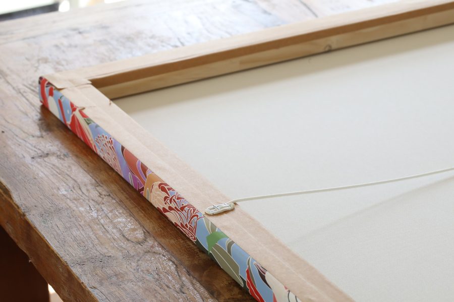 The back of a canvas with framing tape over the staples and a hanging cord fitted